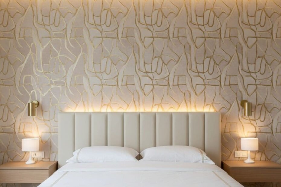 Quarto de casal moderno com papel de parede texturizado em tons neutros, cabeceira estofada e iluminação indireta sofisticada.